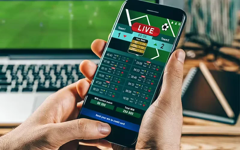 Persona concentrata con cuffie, che guarda quote sportive live su laptop con accenti neon dinamici e interfaccia scommesse futuristica