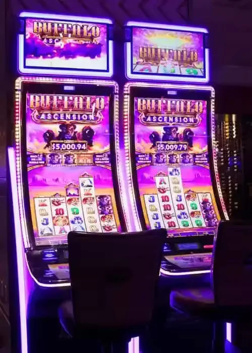 Sleek laptop displaying rising multiplier game interface on dark surface, surrounded by luminous casino chips and roulette elements under dramatic lighting